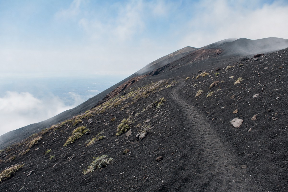 Hikers on a black volcanic sand trail on Mount Etna's slopes